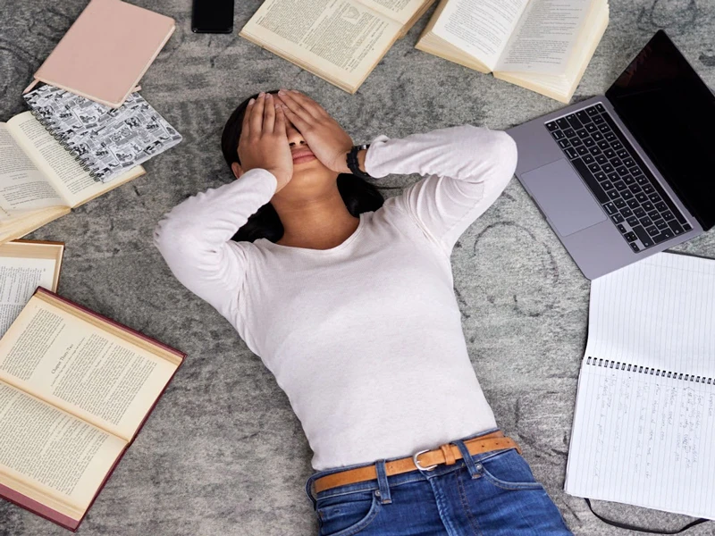 stressed out girl lying on the floor next to her school books and laptop